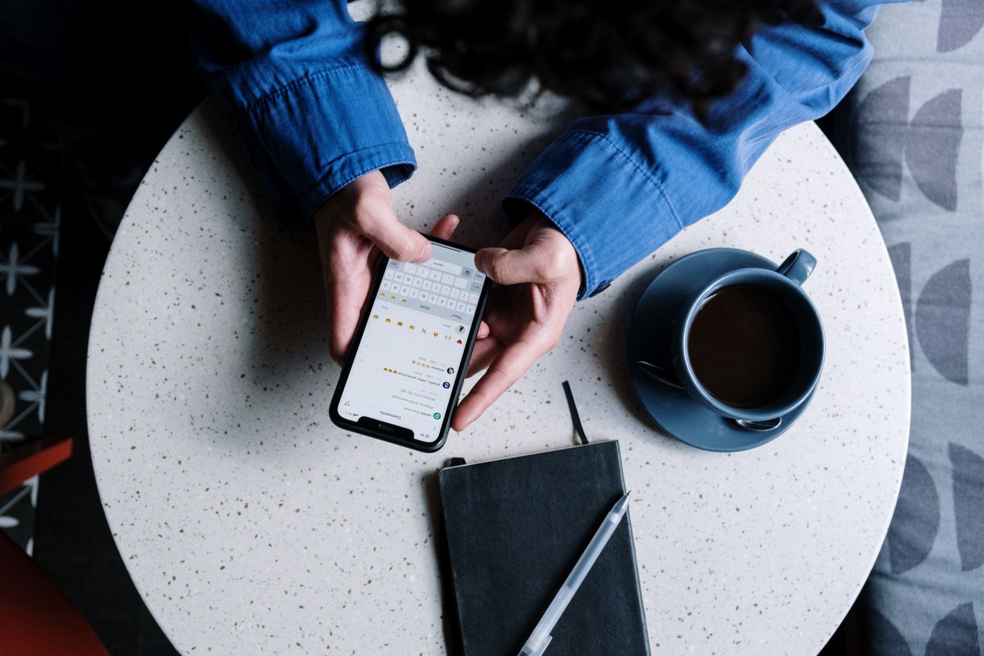 Person using a smartphone beside a notebook and cup of coffee