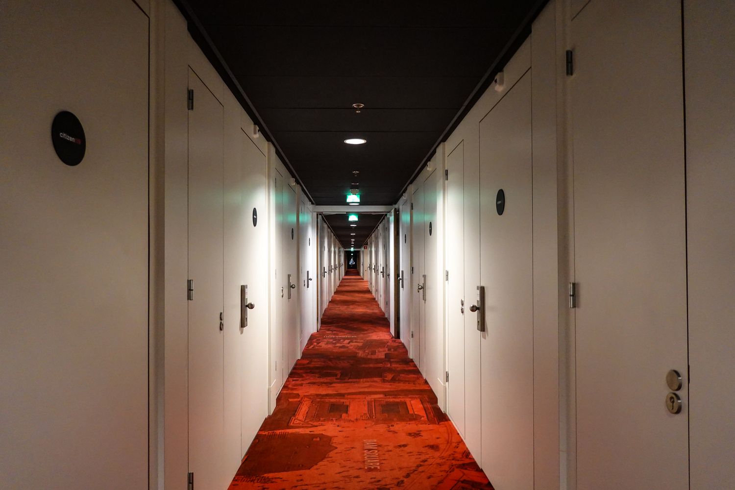 Symmetrical hotel corridor with red carpet and rows of closed white doors