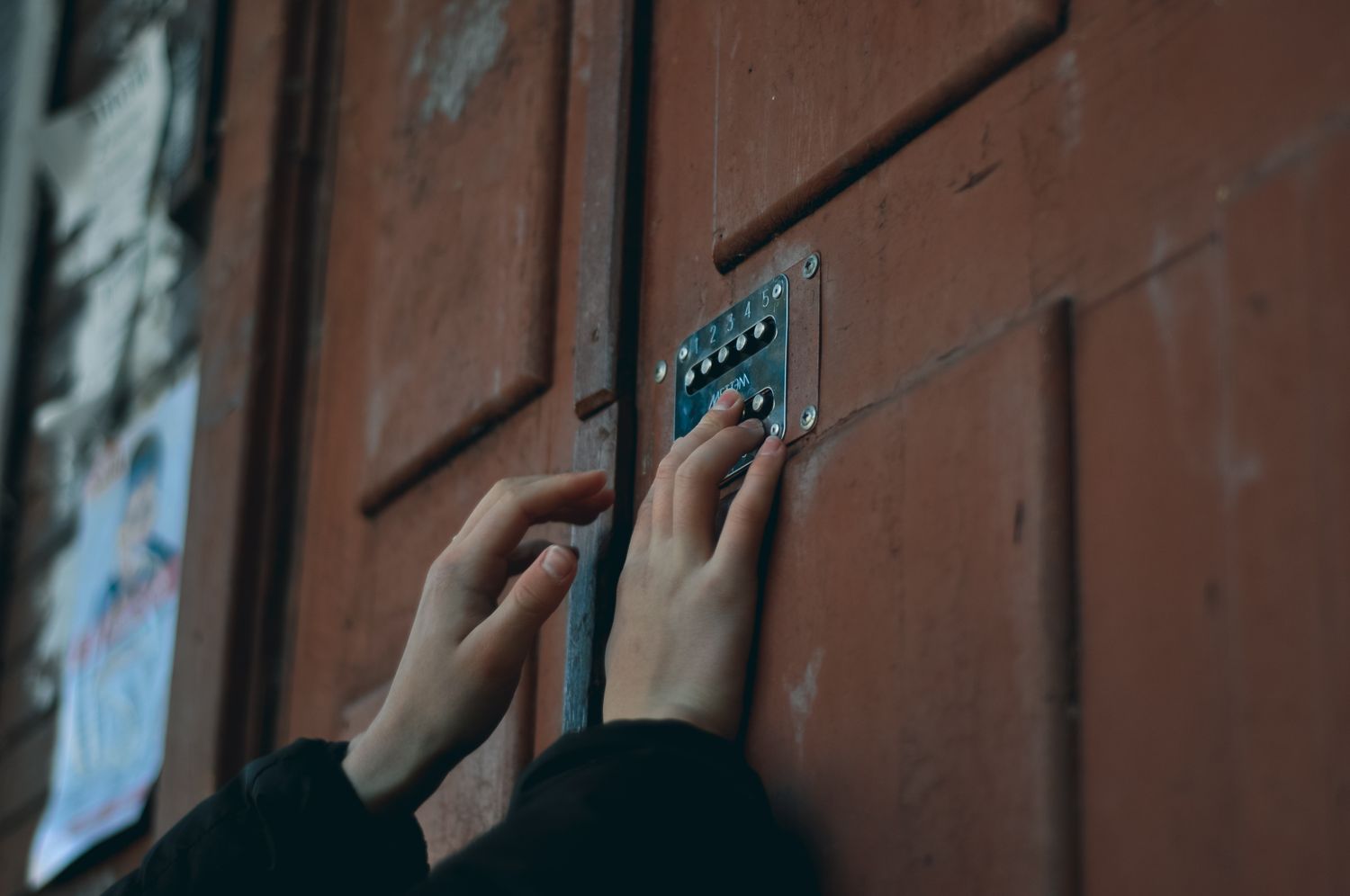 Hands pressing a code into a keypad lock on a wooden door